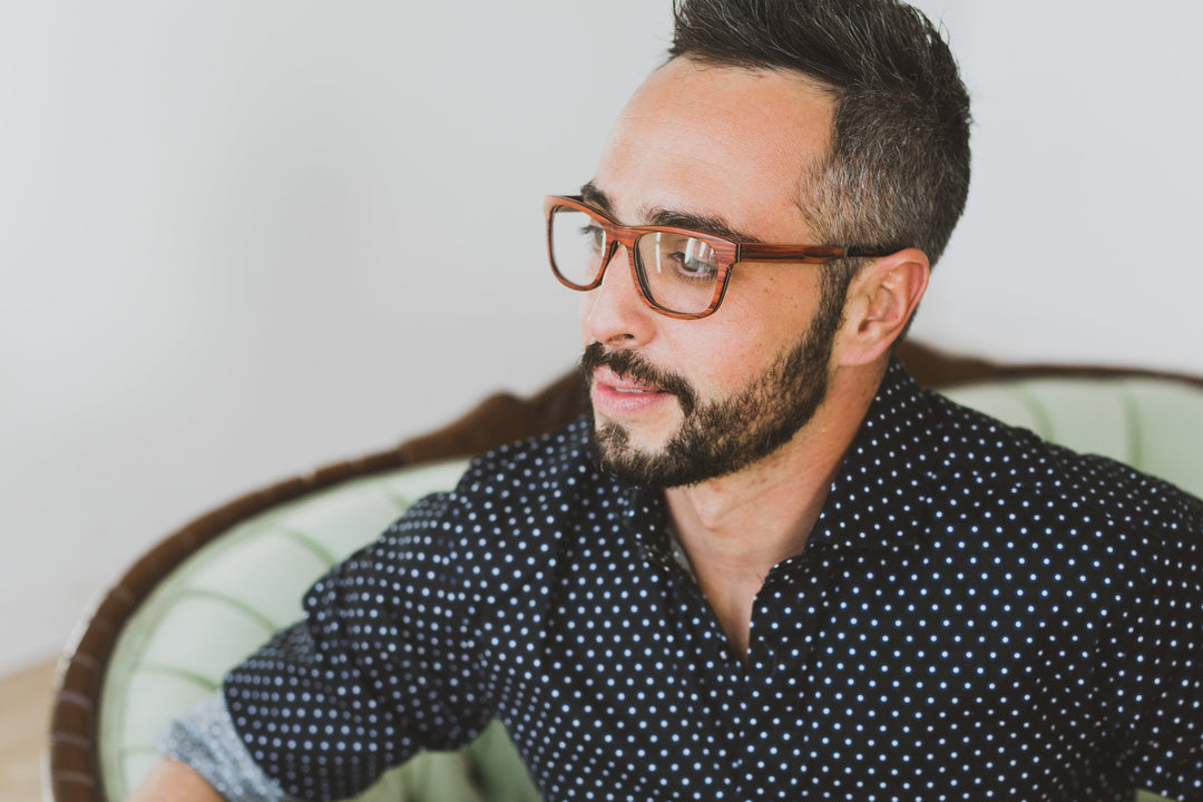 man gazing to his right, wearing rosewood eyeglasses.