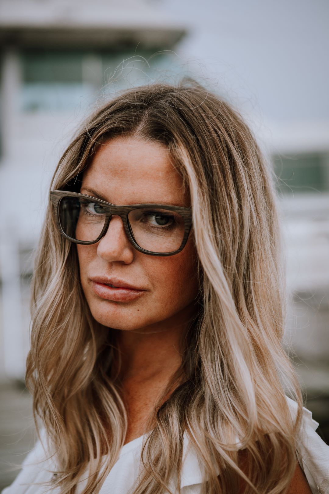 blonde woman wearing black oak wood glasses, looking at camera.