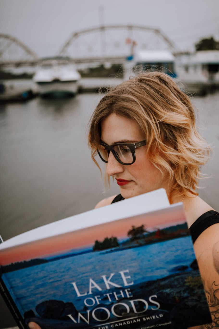 Woman reading a book, wearing Keepwood black oak eyeglasses. 