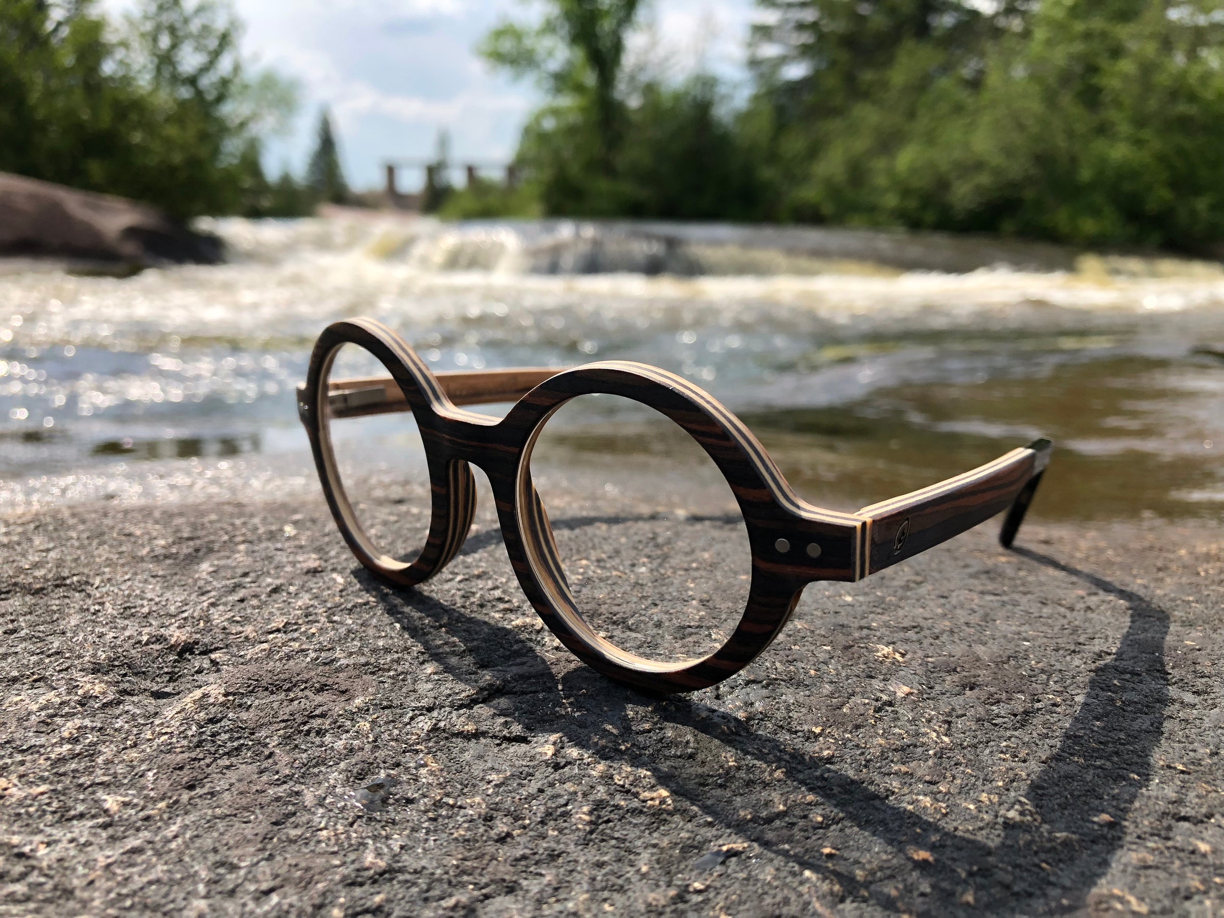 round wood glasses lying on rock, with waterfall in the background.