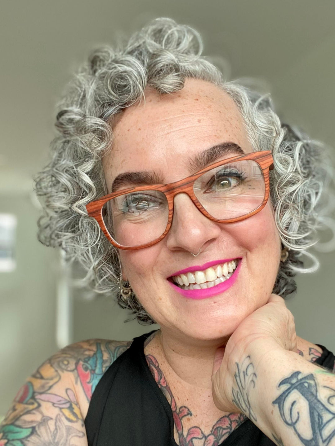 Smiling tattooed woman wearing rosewood eyeglass frames.